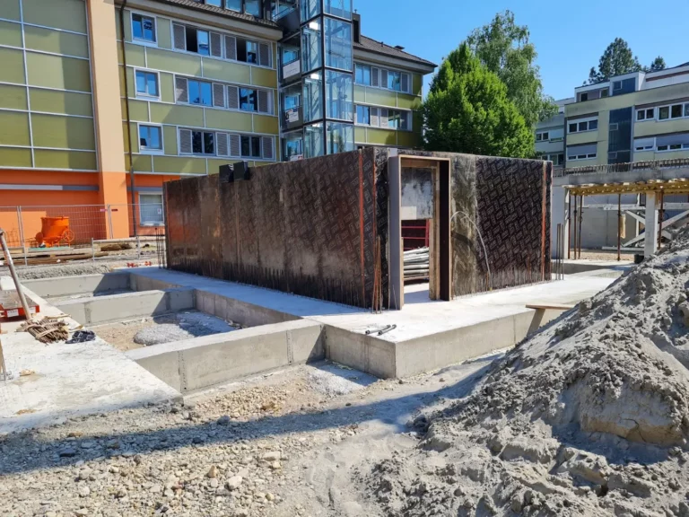 Im Bau befindliches Betongebäude mit Nebengebäuden, Erdhaufen und nahegelegenen Wohnungen.
