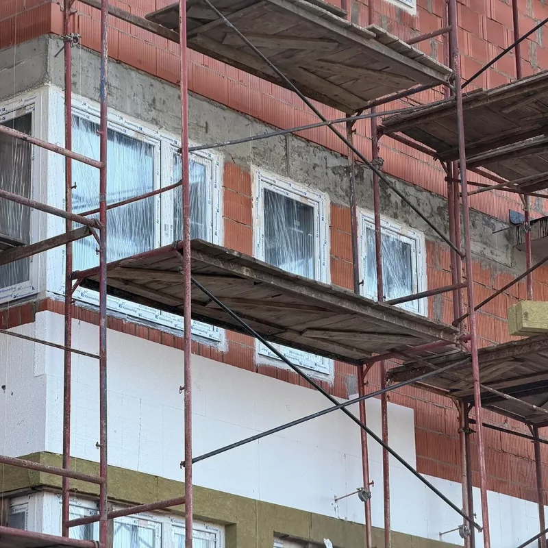 Für Renovierungsarbeiten aufgestelltes Gerüst neben einem Gebäude mit sichtbaren Fenstern.