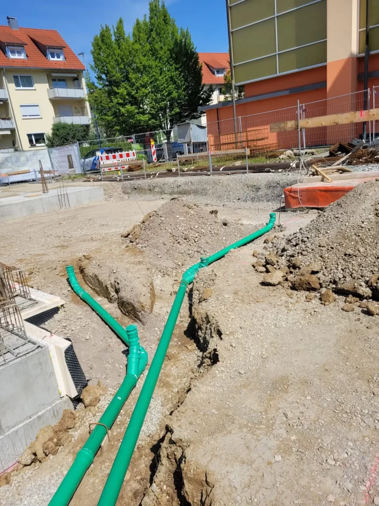 Grüne Rohre für die Entwässerung, die bei Erdarbeiten in der Nähe von Gebäuden in einem Graben verlegt wurden.