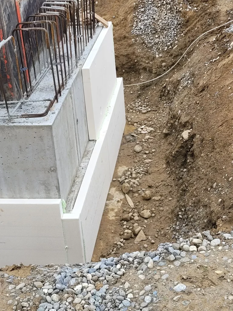 Fundamentwand mit Dämmung, Bewehrung und Erdarbeiten auf einer Baustelle.