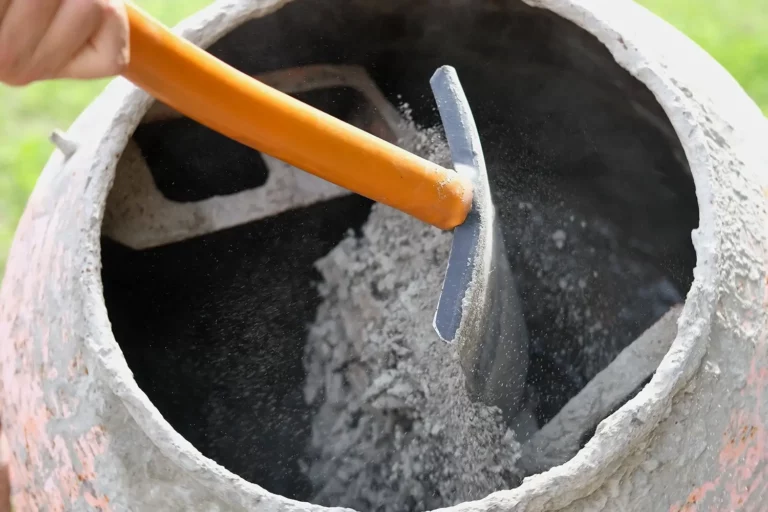Schaufel mit orangefarbenem Stiel, mit der graues Zementpulver für Maurerarbeiten geschöpft wird.