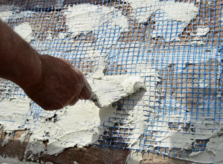 Bei Maurerarbeiten wird Putz von Hand auf eine Wand mit blauem Gewebe aufgetragen.